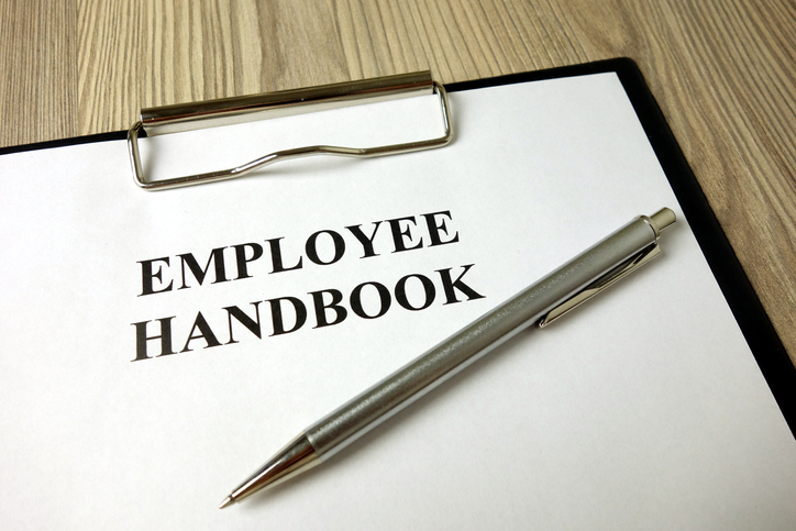 Employee handbook on a desk with a pen resting on top of it during employee handbook monitoring.