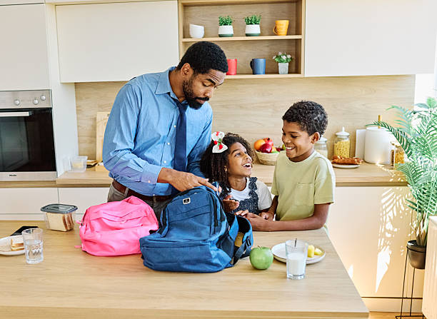 Father businessman helping son and daughter to get ready for school, holding smartphone and having a phone call, helping him with backpack and books, and making snack sandwich in the kitchen leaving home